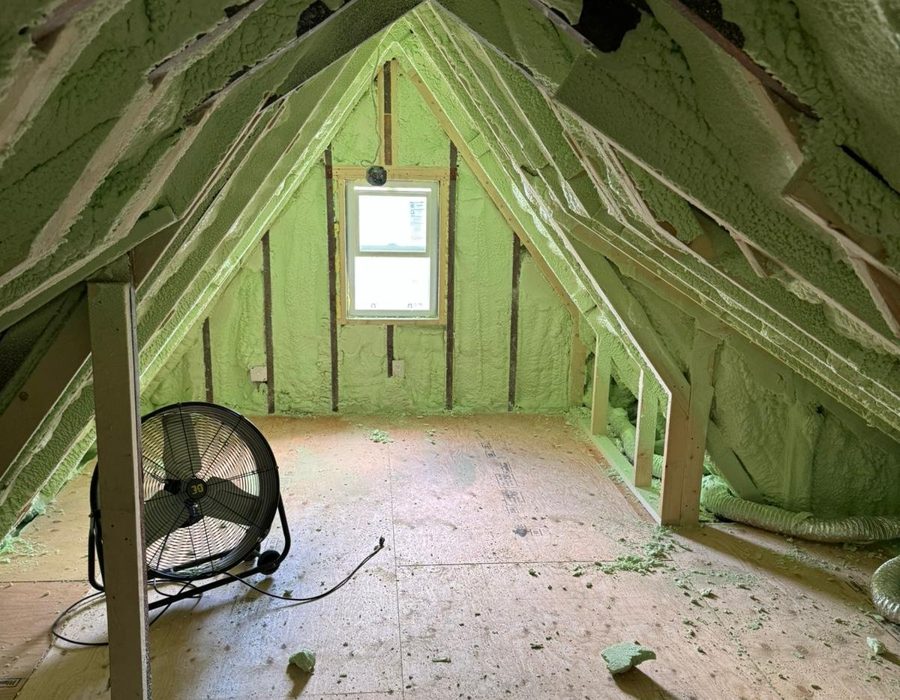 Exposed attic framing with spray equipment staged on the floor